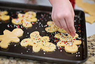 person sprinkling cookies on black tray