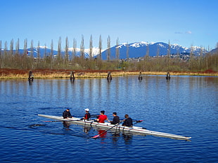 five person on boat floating on rippling body of water over looking mountain and trees