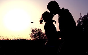 man and woman kissing under the clear sky during sunset