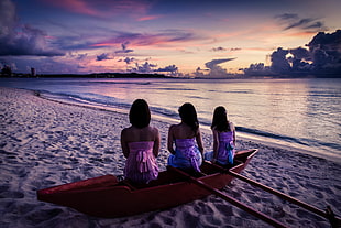 three woman riding in canoe on sand near body of water