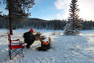 man wearing red knit cap making fire on snowy field during daytime