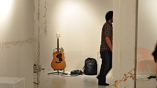 man in black jeans standing near brown acoustic guitar
