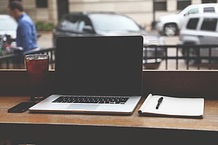 turn off  black and gray laptop computer beside clear cut drinking glasses and phone with notebook and pen on table