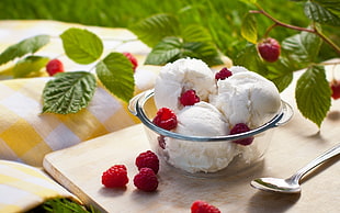 scoops of ice cream on clear glass bowl on top of wooden surface near stainless steel spoon