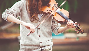 person wearing gray sweater playing a violin during daytime