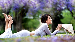 woman lying on her belly holding white hat on purple flower field at daytime
