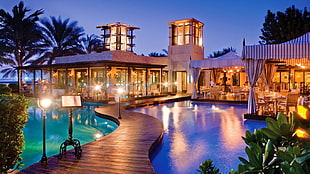 brown wooden dock at middle of pool, building, palm trees, lights