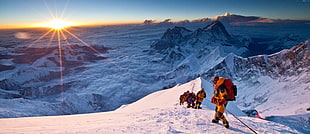 people climbs on snowy mountain during sunrise