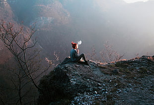 woman sitting on top of mountain while smoking