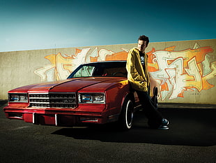 man wearing yellow jacket leaning red car in front of wall artwork HD wallpaper