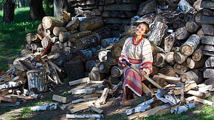 woman in white, red and brown traditional dress sitting on firewood lot