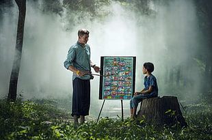 man teaching a child sitting on tree trunk during daytime HD wallpaper
