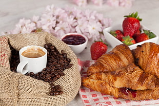 coffee in cup with coffee beans on table with strawberries and croissant