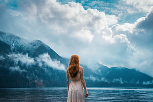 woman in white dress in front of bodies of water under cloudy sky at daytime