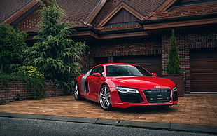 red coupe parked beside brown house during daytime