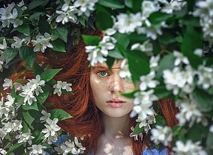 red haired girl beside the white flowery bush