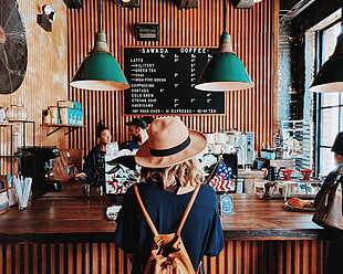 woman in blue shirt with brown sun hat near coffee shop counter