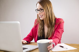 woman holding a coffee mug on office table while working use a silver MacBook in white wall paint room