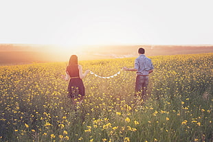 man and woman in clothing standing on yellow flower field during daytime