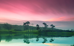 landscape photography of body of water near grass field under red sky