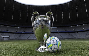 low-angle photography of silver soccer trophy cup near soccer ball on stadium