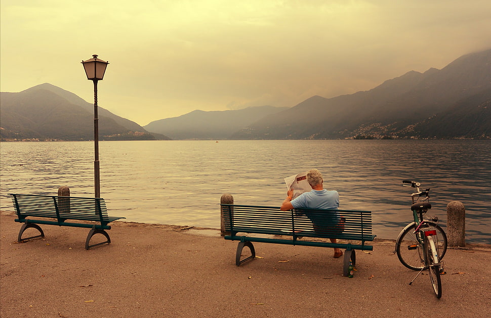 man in blue shirt sitting on bench while facing on bay HD wallpaper