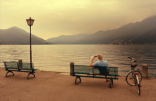 man in blue shirt sitting on bench while facing on bay HD wallpaper
