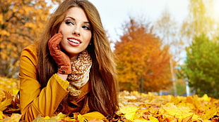 woman wearing beige coat laying on a bunch of dried leaves