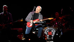 man holding red electric guitar knelling on stage