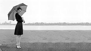grayscale photo of woman wearing black long-sleeve midi dress holding umbrella near water formation