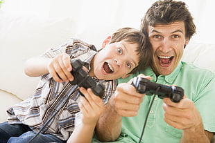 man and boy holding dualshock 3 controllers during daytime