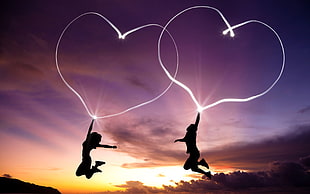 silhouette of two person jumping while holding heart shaped neon light