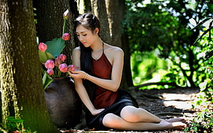 woman in red sleeveless shirt and black skirt sitting near brown flower vase