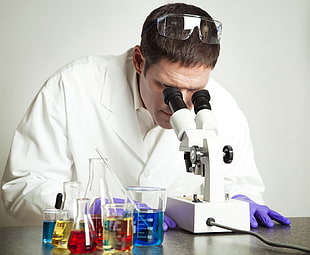 man in white lab gown looking at microscope