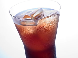 brown drink with ice in clear glass