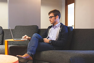 man wearing black zip hoodie using laptop computer sitting on black fabric sofa HD wallpaper
