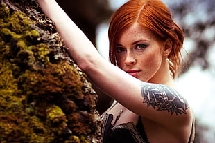 woman with flower arm tattoo standing next to rock