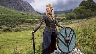 woman in medieval clothes holding shield and sword in the middle of green grass field