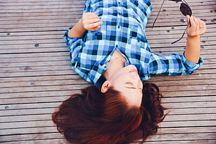 woman in blue flannel lying on wooden dock while holding sunglasses