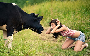 woman wearing red, black, and white plaid crop top and blue denims short shorts mocking black and white cow