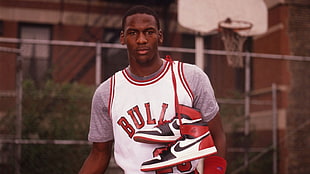 man in white and red Chicago Bulls jersey shirt with pair of white-and-red Air Jordan 1 shoes on hanging on shoulder