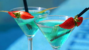 two martini glasses with clear liquid, black straw, and sliced strawberries