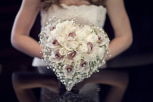 woman holding heart-shaped white and purple petaled flower arrangement