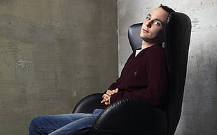 man in brown long sleeve shirt and blue jeans sitting on black leather chair