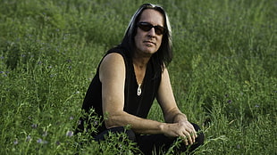 man in black sleeveless top wearing black sunglasses sitting on grass field