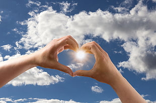 person heart shaped hand sign under white and blue cloudy sky during yellow sunny day