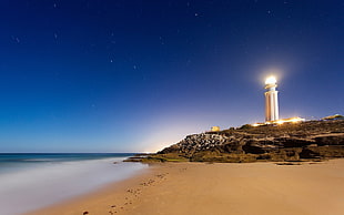 white lighted lighthouse beside body of water