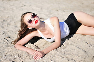 woman in white tank top and black panty lying on sand during daytime