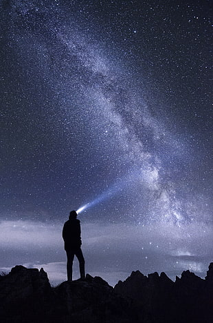 silhouette of man with headlamp standing on mountain under nebula, stars, space