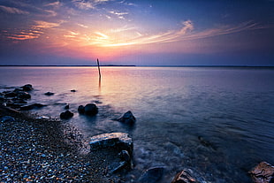 calm sea with stones on seashore under blue sky HD wallpaper